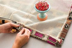 a person is sewing on a table with a vase in the background and colorful beads