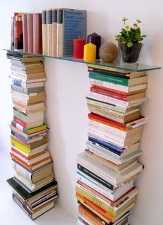 a tall stack of books sitting on top of a shelf next to a vase filled with flowers