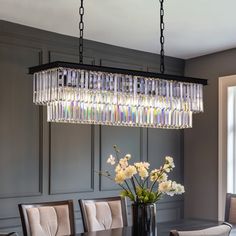 a chandelier hanging over a dining room table with flowers in the vase on it