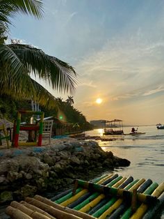 the sun is setting over an ocean with canoes in the water and palm trees