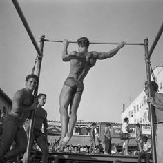 three men are doing pull ups in the middle of an outdoor gym while others watch