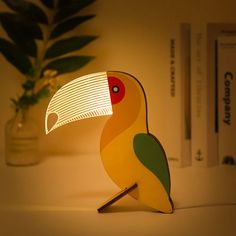 a yellow and green bird lamp sitting on top of a table next to a potted plant