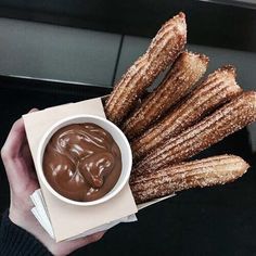 a person holding a box with churros and dipping sauce in it's hand