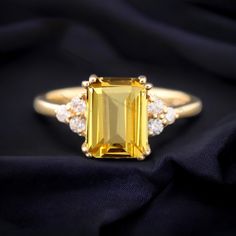 an emerald cut yellow sapphire and diamond ring on a black silk background with gold accents