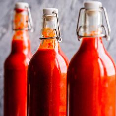 three bottles filled with red sauce sitting on top of a table