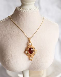 An artisan-made 14K gold-filled pendant, with a Garnet cabochon and faced cubic, is carefully hung from ball chain with a lobster clasp. This captivating pendant, boasting artwork of incomparable skill and a magnificent combination of red Garnet with an orange hue and translucent red Cubic, offers a perfect juxtaposition of poise and dynamism, making it an elitist piece of jewelry. The length of necklaces is approx. 24". Follow me on Instagram: @cubic_jewels Oval Pendant Necklaces With Cabochon For Wedding, Oval Pendant Cabochon Necklace For Wedding, Oval Cabochon Pendant Necklace For Weddings, Victorian Pendant Necklace With Cabochon, Victorian Cabochon Pendant Necklace, Wedding Necklaces With Oval Cabochon Pendant, Antique Cabochon Necklace With Round Pendant, Antique Cabochon Round Pendant Necklace, Yellow Gold Cabochon Necklace For Wedding