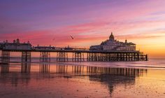 the sun is setting over the beach and pier