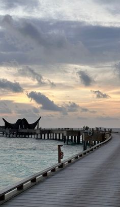 a long pier stretches out into the ocean as clouds loom in the sky above