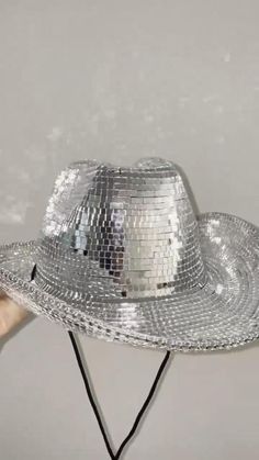 a silver hat is being held up by someone's hand in front of a mirror wall