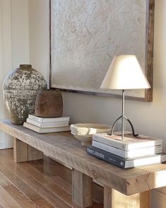 a wooden table topped with books and a lamp next to a painting on the wall