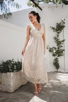 a woman in a white dress is walking down the street wearing sandals and a necklace