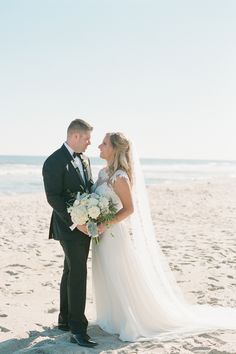 a bride and groom standing on the beach