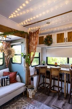 a living area with couch, table and kitchen in the back ground is lit up by string lights