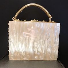 a white purse with gold handles on a black surface