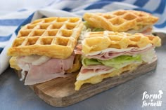 two waffle sandwiches with ham and lettuce on a cutting board next to a blue striped towel