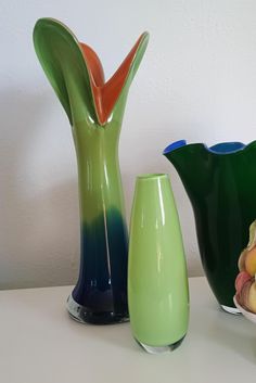 three different colored vases sitting on a white table next to each other and one has a flower in it