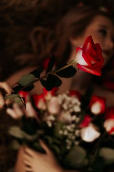 a woman holding a bouquet of red and white flowers in her hands, with the background blurry