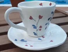 a coffee cup and saucer sitting on a table next to a swimming pool in the background