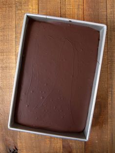 a square pan filled with chocolate frosting on top of a wooden table