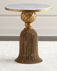 a table with a tasseled base and gold leaf decoration on it's top