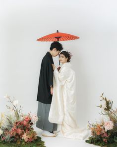 a man and woman are standing under an umbrella in front of some flowers with their faces close to each other