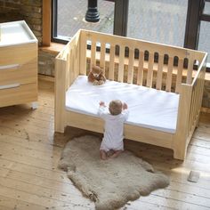 a baby standing in front of a wooden crib