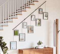 a wooden cabinet under a staircase with pictures on the wall next to it and a potted plant