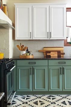 a kitchen with green cabinets and black stove top in the center, on a patterned tile floor