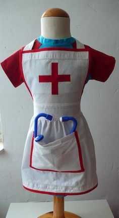 an apron with a red cross on the front and blue scissors in the back, sitting on a mannequin