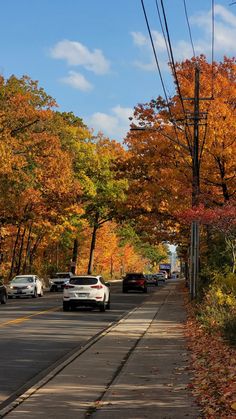 cars are driving down the road in front of trees with orange and yellow leaves on them