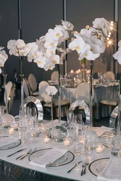 the table is set with silverware and white flowers in tall vases on each side