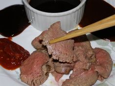 a white plate topped with meat and sauce next to a bowl of dipping seasoning