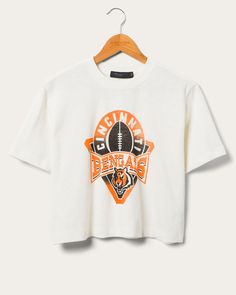 Step up your Bengals game-day look with the Women's Bengals Mock Neck Crop Tee! This NFL-licensed apparel combines Cincinnati Bengals pride with a sleek mock neck design. With its flattering crop cut and sporty logo, you'll stand out in style while cheering for your team. Perfect for fashion-forward football fans! Shop the rest of our Women's NFL Collection HERE. Cincinnati Bengals Sweatshirt, Sporty University Logo T-shirt With Crew Neck, Streetwear Top With Team Logo, Team Logo Tops For Streetwear, Graphic Tee With Team Logo For Fans, Graphic Tee With Team Logo For Fan Gear, Team-colored Tops With Team Name For Streetwear, Fan Gear Graphic Tee With Team Logo, Sports Fan Tops With Team Logo For Sports Events