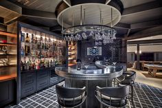 a bar with lots of bottles and glasses hanging from it's ceiling, surrounded by chairs