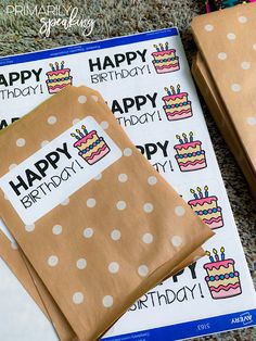 two brown bags with happy birthday stickers on them sitting next to some wrapping paper