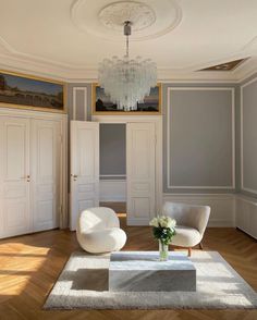 a living room with two white chairs and a chandelier hanging from the ceiling