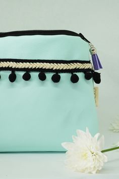 a blue purse with black tassels and a white flower on the table next to it