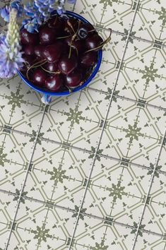 a blue bowl filled with cherries sitting on top of a tiled floor next to purple flowers