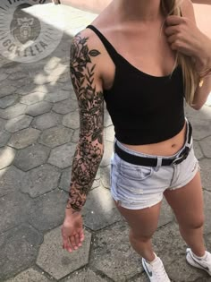 a woman with tattoos on her arm is standing in front of a brick walkway and holding an umbrella