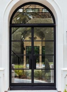 an arched glass door in front of a white stucco building with black doors and windows