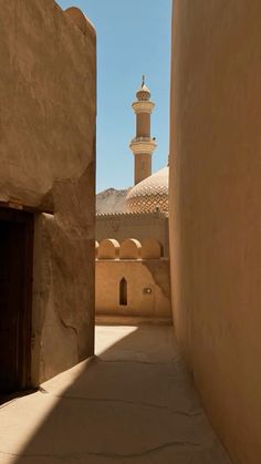 an alley way between two buildings with a bell tower in the background and a blue sky