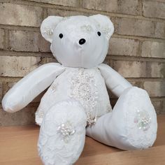 a white teddy bear sitting on top of a wooden table next to a brick wall