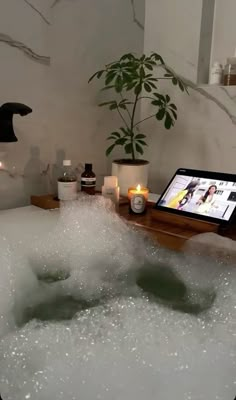 a tablet sitting on top of a bathtub filled with bubbles and candles next to a potted plant