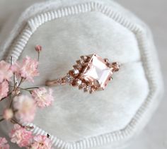 a pink diamond ring sitting on top of a white pillow next to flowers and a flower vase