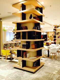 a room filled with lots of tables and chairs next to a tall book shelf that has books on it