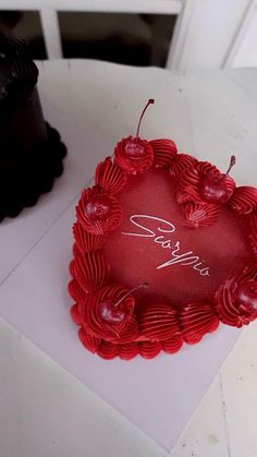 a red heart shaped cake sitting on top of a table next to a black cake