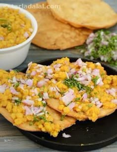 some food is sitting on a black plate and next to crackers, bread, and a bowl