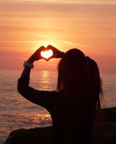 a woman making a heart shape with her hands on the beach at sunset or sunrise