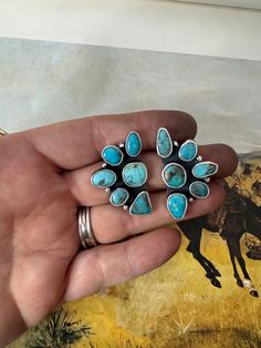 a person holding a ring with turquoise stones in their hand and a painting on the wall behind them