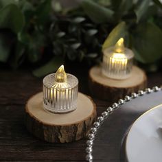 two clear glass candles sitting on top of wooden slices next to a plate and silverware